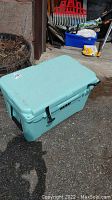Turquoise Yeti cooler placed outdoors on asphalt near planters and garden tools