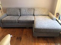 Full view of grey L-shaped sofa with three seat cushions and chaise extension on the right, placed on wooden floor.