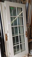 Photo of one beige wood door with multiple rectangular glass panels inserted, brass/gold handle, and part of wood frame.