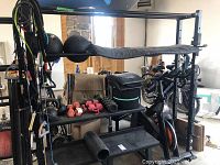 Front view of heavy metal fitness frame with bench, weights, resistance bands, and exercise bike visible.