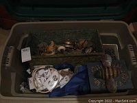 Photo of a tote showing a green metal box filled with brass hardware pieces, white electrical covers, blue cloth, and a bee decorative item on a painted stone.