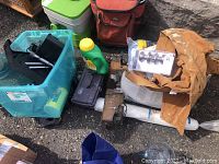 Photo showing assorted hardware items including tools, toolbox, a plastic bottle of green liquid, a packaged door knob set, and brown plastic coated coveralls with paint stains.