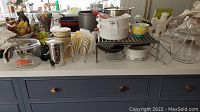Wide view showing various glass jars, ceramic canisters, bowls, metal lid holder, hand mixers, and miscellaneous kitchen items on a countertop.