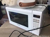 White Panasonic microwave oven shown from the side and front with keypad and digital display. Microwave appears to need cleaning.
