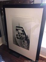 Full view of large framed black-and-white print showing man in uniform and dog aboard a boat from overhead angle.