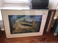 Overall view of three framed art pieces stacked against a wall.