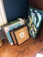 Full view of all artwork stacked together, showing two canvases including fish painting and dog canvas, plus five framed prints.