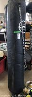 Full view of tall black punching bag with chain hanging attachment and Round One Boxing logo.
