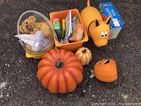 Overview of toys, farm hopper, books and artificial pumpkins laid on ground.