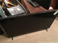 Large flat-screen TV on carpet, shown from front with screen off.