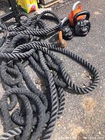 Photo of black fitness battle ropes laid on asphalt with rubber handles visible.