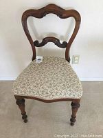 Front view of antique wooden chair showing the carved top rail and upholstered floral seat.