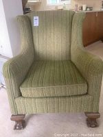 Front view of the green fabric armchair showing the cushioned seat, patterned upholstery, and carved wooden claw feet with casters.