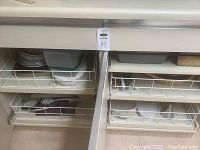 White kitchen drawers and cabinets pulled out showing assorted bowls, bakeware, and storage containers