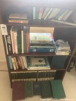 Wide view of shelves filled with vintage books and music tapes, showing a large collection of garden, cookbooks, and floral-themed books, plus few cassette tapes.