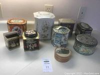 Nine assorted collectible tins on a counter with outlet and light switch in the background.