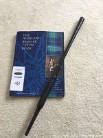 The Highland Bagpipe Tutor Book with blue cover showing bagpipe diagrams and tartan, alongside a black plastic practice chanter.