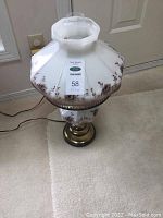 Front view of hurricane lamp showing octagonal white glass shade with floral design, brass base, and power cord.