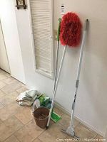 Photo showing cleaning items including a mop with red microfiber head, a dust mop, cleaning cloths, and a waste basket.