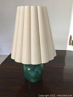 Full lamp showing green ceramic base and beige pleated fabric shade