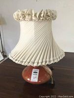 Photo showing full lamp with ceramic base and pleated fabric lampshade with ruffled edges.