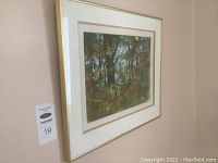 Framed watercolour painting hanging on a wall, showing a landscape of a forest with autumn colors.