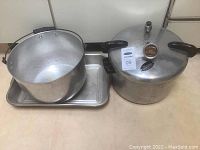 Photo showing the pressure cooker with lid, aluminum pot, and rectangular bake pan on a flat surface.