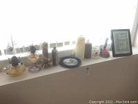 Two glass oil lamps, assorted pillar candles in holders, winter scene plate, figurine, and framed print on window ledge