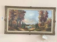 Full view of the framed oil painting of an autumn landscape by Peter Veraz showing colorful trees, water body, distant mountains and sky.