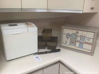 Full lot on kitchen counter including Philips bread maker, three decorative bread pans, wooden bread box, and knife.