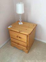 Front view of pine nightstand with two drawers and lamp on top in a corner of a room
