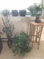 Full view of bamboo plant stand with pots and artificial/dried plants arranged on and around it near a window.