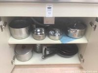 Pots and pans inside a cabinet shelf, featuring multiple pots and stainless-steel bowls.