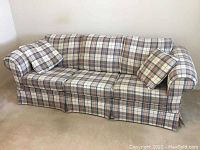 Side angle view of the vintage Sears hide-a-bed couch showing plaid fabric upholstery and a matching pillow.