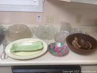 Wide shot showing the entire set of serve ware items on a countertop including glass, crystal, wooden, plastic, and ceramic pieces.