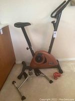 Sirius Fitness stationary bike, orange and black, angled left side view showing seat, pedals, and base supports