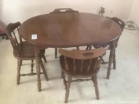 Round wooden dining table with four matching chairs shown assembled together on carpeted floor.