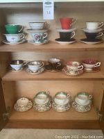 Photo of multiple vintage teacup sets displayed on shelving including various colors and floral patterns.