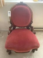 Front view of vintage parlour chair showing carved wood frame and red velvet seat and backrest with wear marks.