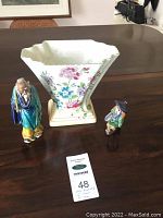 Photo of vintage Art Deco stepped Tuscan vase with two small Chinese statuettes on a wooden table.