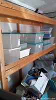 Shelving with clear plastic bins with green lids and white plastic bin, arrangement of bins on wooden shelving in basement area.
