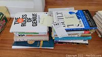 Stack of business books on the floor showing titles like 'The 46 Rules of Genius' and 'Business Model Generation'.