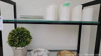 Shelf showing four white flameless candles on the top shelf with decorative dishes and faux plant below