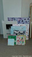 Photo showing nine pieces of canvas art and one framed Channel cologne print arranged on the floor with varying floral and abstract designs in multiple sizes.