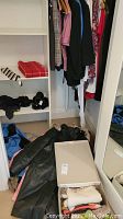 Photo of ladies clothes hanging on wooden hangers in a closet, visible black leather coat and other clothing items.