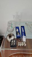 View of full lot on glass-top table including crystal items, silver plated salt and pepper shakers, silver tray, and wedding cake knife and server in blue boxes.