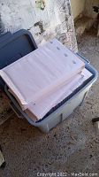 White bubble mailer envelopes stacked inside a gray plastic storage bin in a basement setting.