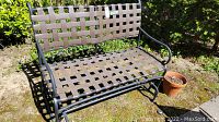 Angle view of metal garden glider bench showing woven metal strap seat and backrest on tubular metal frame with outdoor setting.