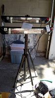 Two Sundear Star stand-up heaters mounted on tripod stands shown in a basement area with papers and box in background.