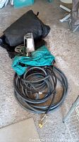 Overview photo showing all items: deck garden hose coiled, hose nozzle, green tarp, and black BBQ cover.